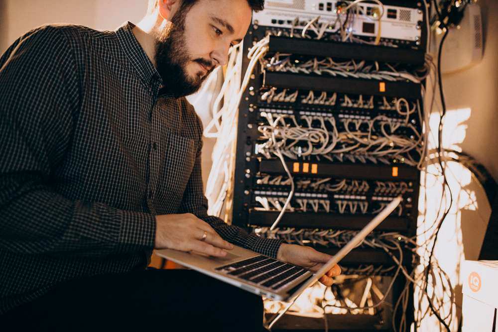 Egy férfi laptopot használ egy szerverkabinban.