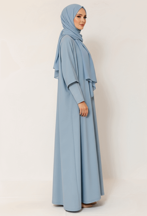 Elegant woman in light blue modest dress and hijab, standing against a plain background.