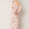 Elegant woman in floral modest dress with beige hijab, standing against a plain background.