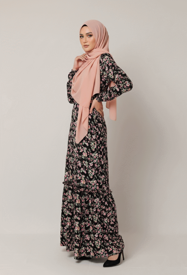 Elegant woman in a floral maxi dress with a blush pink hijab, standing against a neutral background.