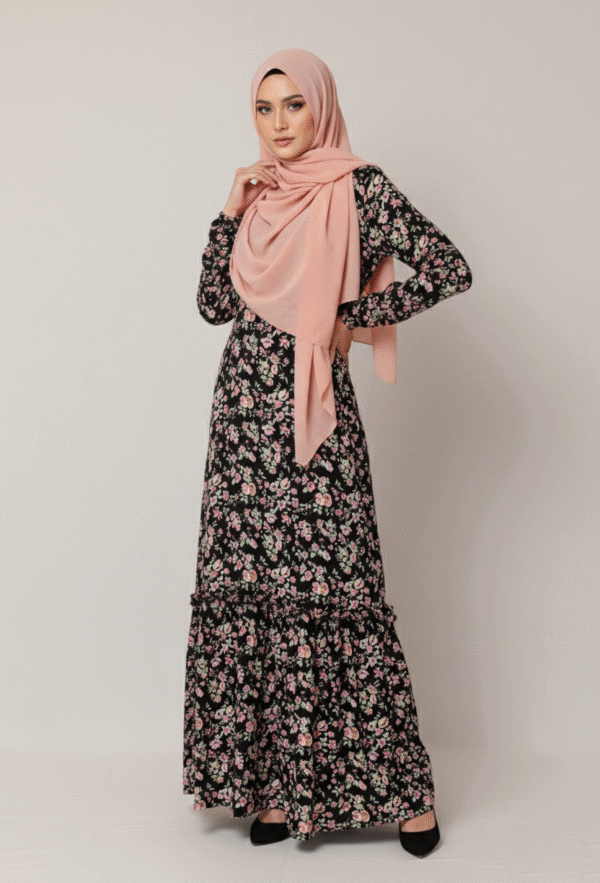 A woman wearing a floral maxi dress and a pink hijab, standing against a plain background.