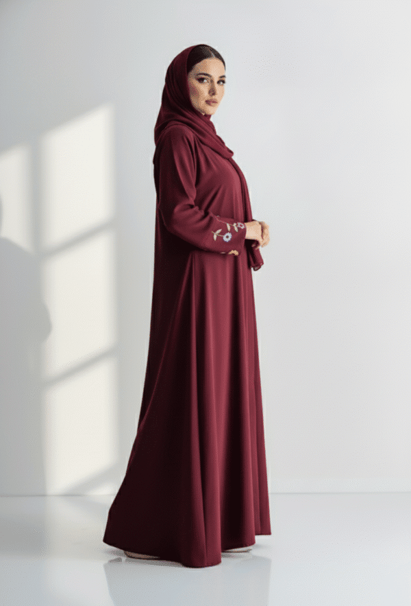 Woman wearing a maroon abaya with embroidered sleeves, standing against a white background.
