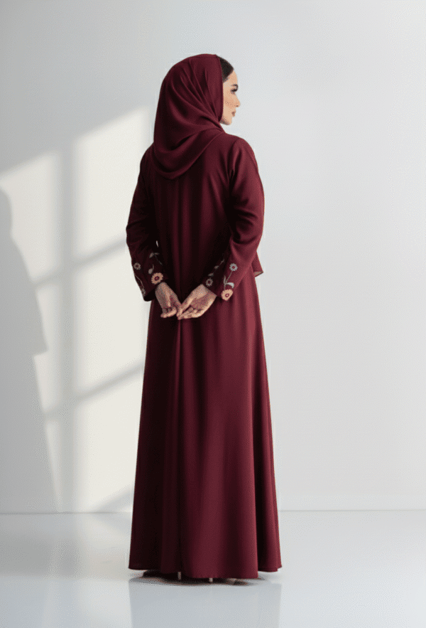 Woman in maroon abaya with embroidered sleeves, standing sideways against a white background.