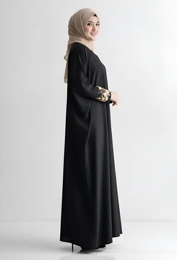 Woman wearing a black abaya with gold embroidery on sleeves, standing sideways.