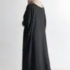 Woman wearing a black abaya and beige hijab, standing against a white background.