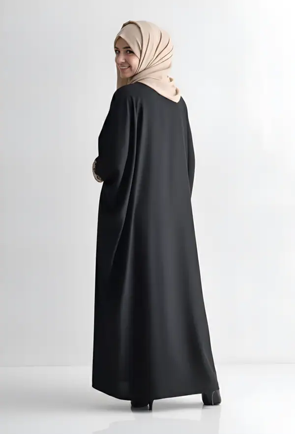 Woman wearing a black abaya and beige hijab, standing against a white background.