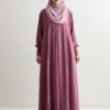 Woman in pink abaya and hijab standing against white background.