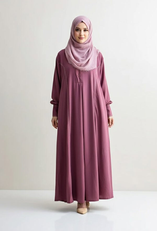 Woman in pink abaya and hijab standing against white background.