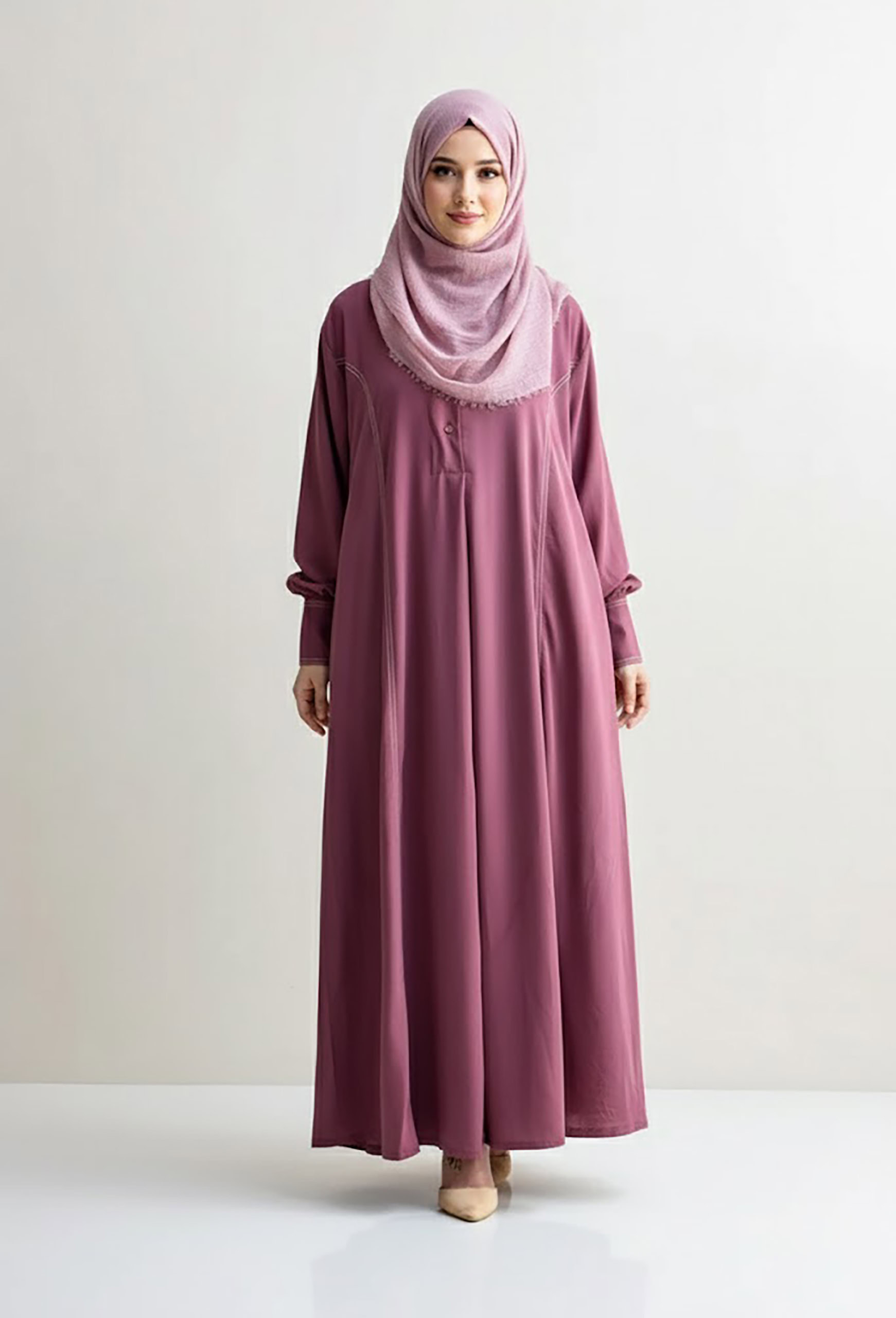 Woman in pink abaya and hijab standing against white background.