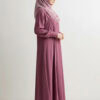 Woman in pink abaya and hijab standing sideways against a plain background.