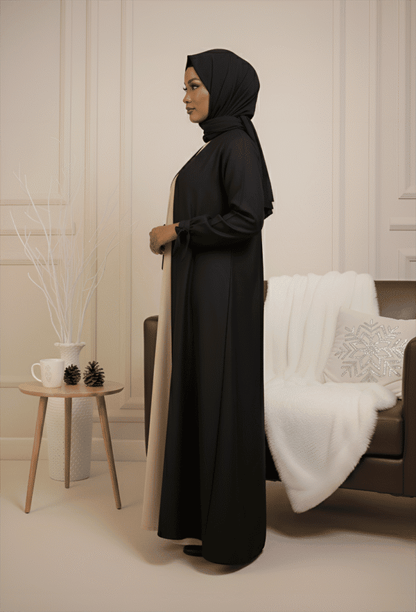 Stylish woman wearing black and beige abaya with hijab, elegant decor for modest fashion showcase.