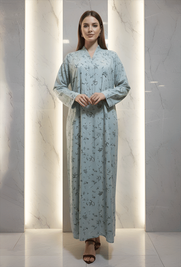 Woman in light blue embroidered dress standing against marble wall.