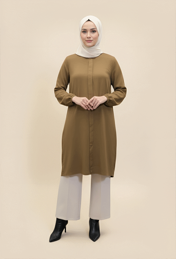Woman wearing a stylish brown modest dress and white hijab, standing confidently against a neutral b.