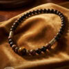 Handcrafted beaded necklace featuring dark wooden beads and gold accents, displayed on a soft velvet.