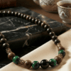 Handmade beaded necklace with green and black beads on a beige fabric background.