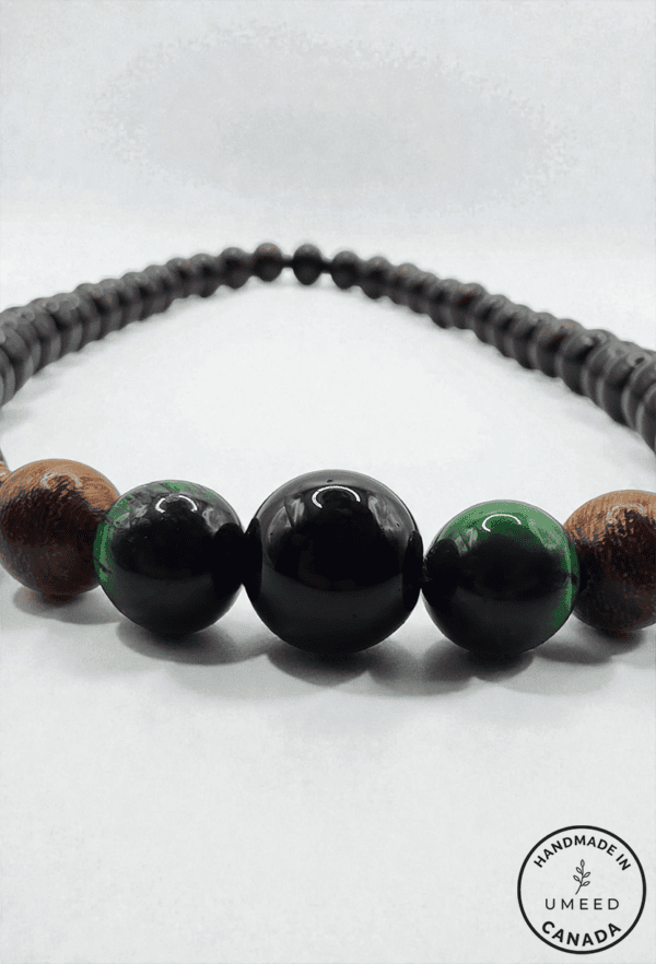 Handmade beaded necklace with black and green beads and wooden accents.