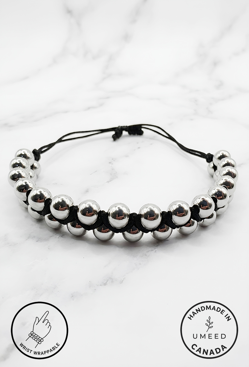 Elegant silver beaded bracelet with adjustable black cord on marble surface.
