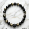 Black and gold beaded bracelet with a lava stone centerpiece on a white marble background.