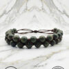Handmade beaded bracelet with green beads and leather cord on marble background.