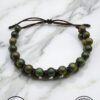 Handmade green beaded bracelet with adjustable cord on marble surface.