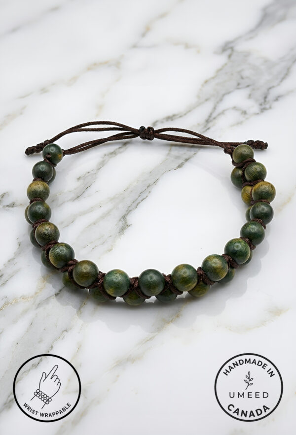 Handmade green beaded bracelet with adjustable cord on marble surface.