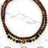 Elegant handmade wooden beaded necklace with gold accents on white marble background.