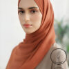Elegant woman wearing a rust-colored hijab, looking confidently at the camera.