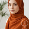 Beautiful woman wearing rust orange hijab with subtle sparkles, light makeup, and a calm expression.