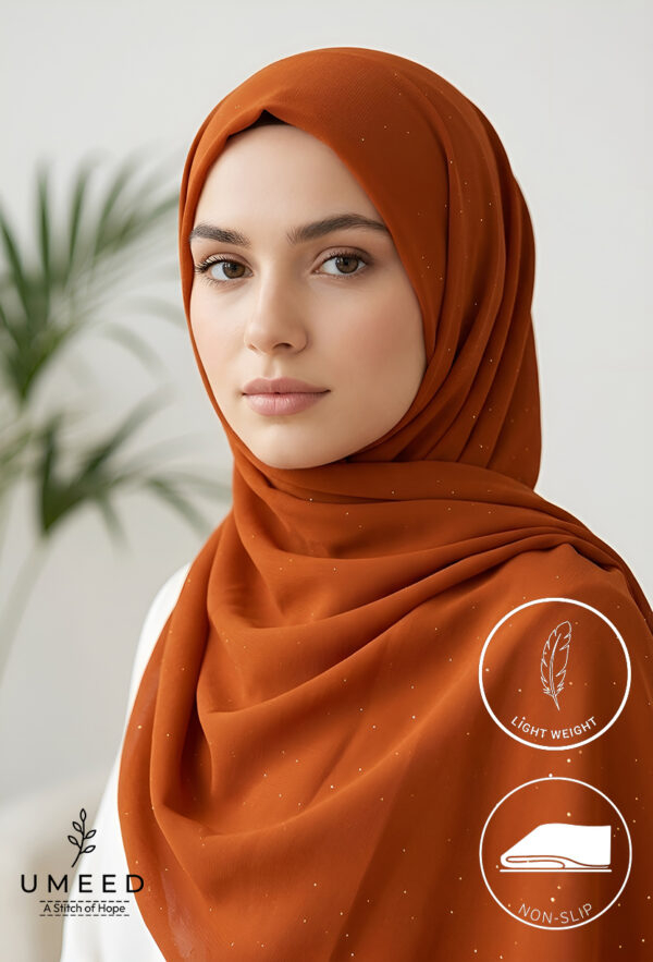 Beautiful woman wearing rust orange hijab with subtle sparkles, light makeup, and a calm expression.
