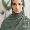 Elegant woman wearing a green hijab with a blurred plant background.