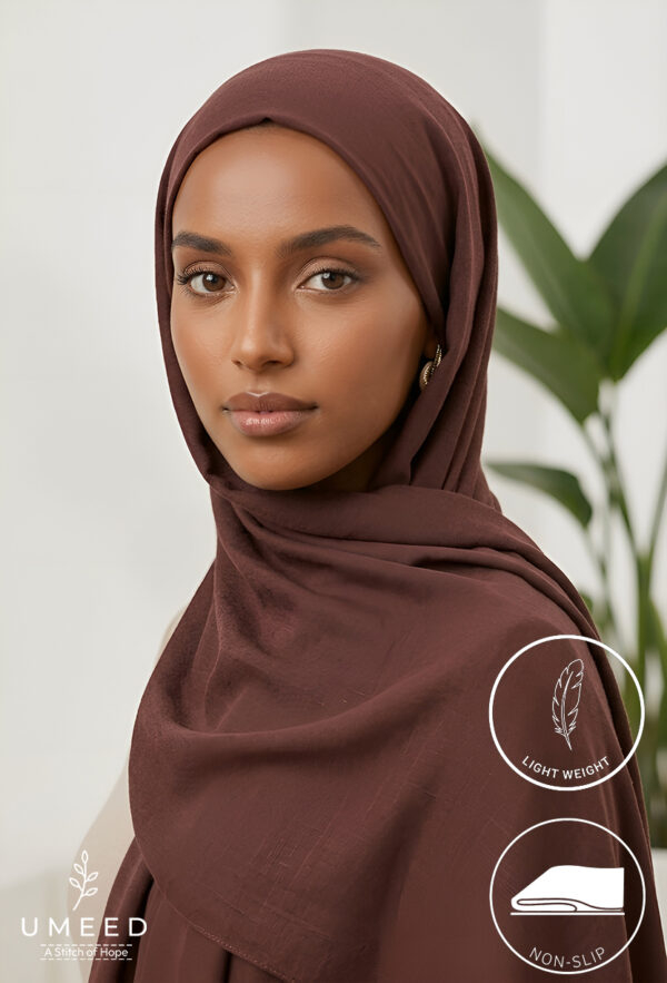 Elegant woman wearing a brown hijab with a light background and green plant.