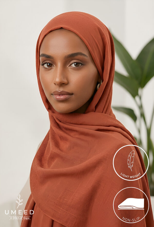 Elegant woman wearing a rust-colored hijab with a neutral background.