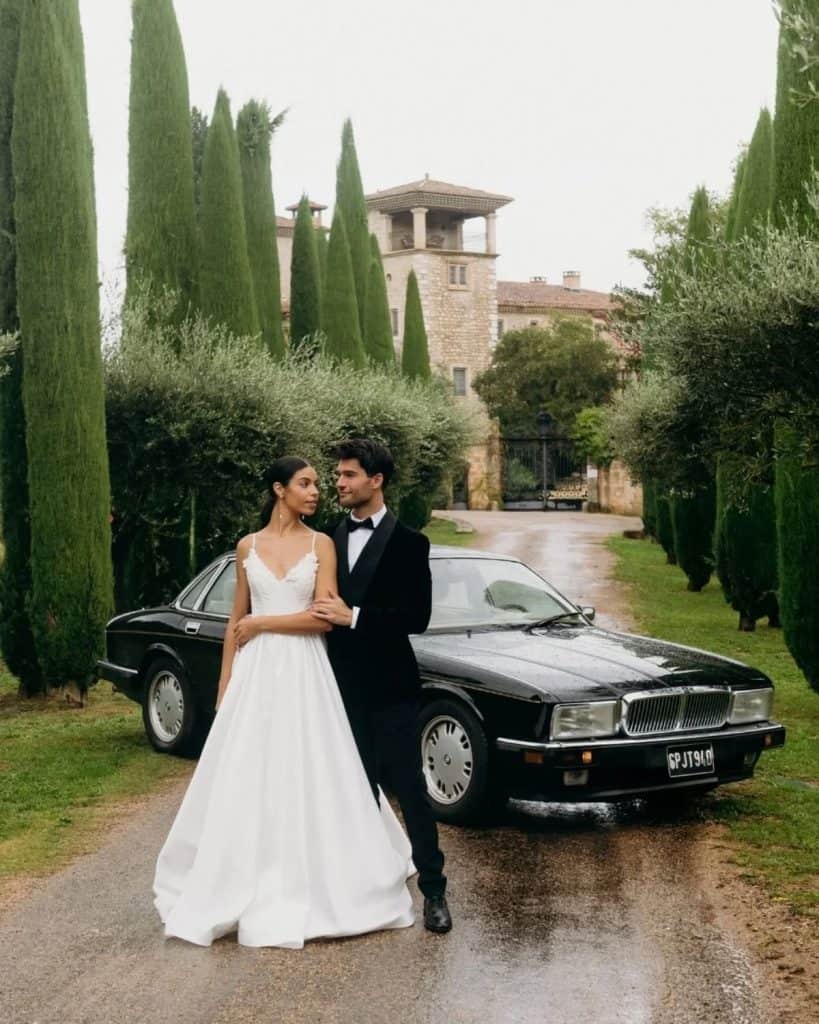 Luxurious wedding couple with car at elegant estate, picturesque setting, romantic celebration, upscale event, beautiful outdoor venue.