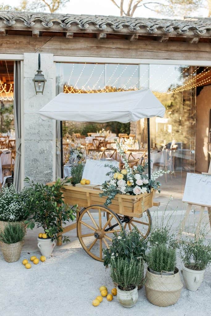 Rustic outdoor wedding reception setup with floral cart and string lights at UpEventi.