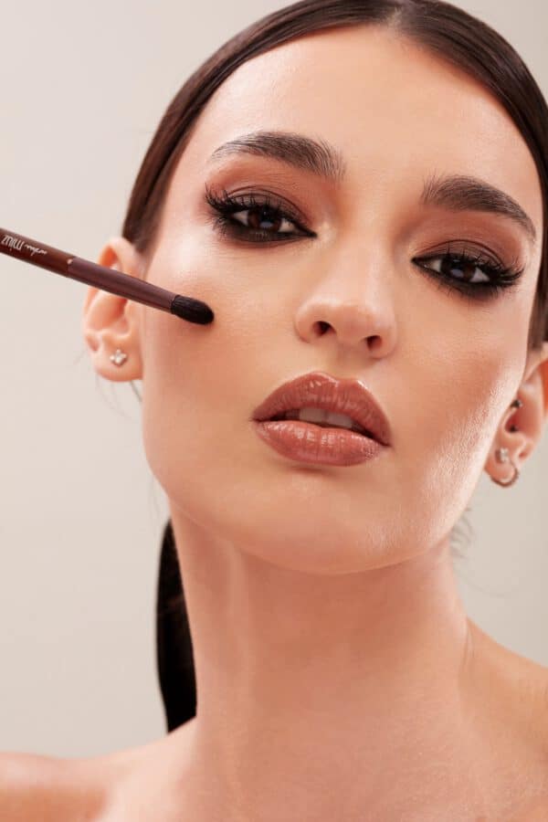 Imagine cu o femeie aplicând machiaj pe ochi cu o pensulă fină.