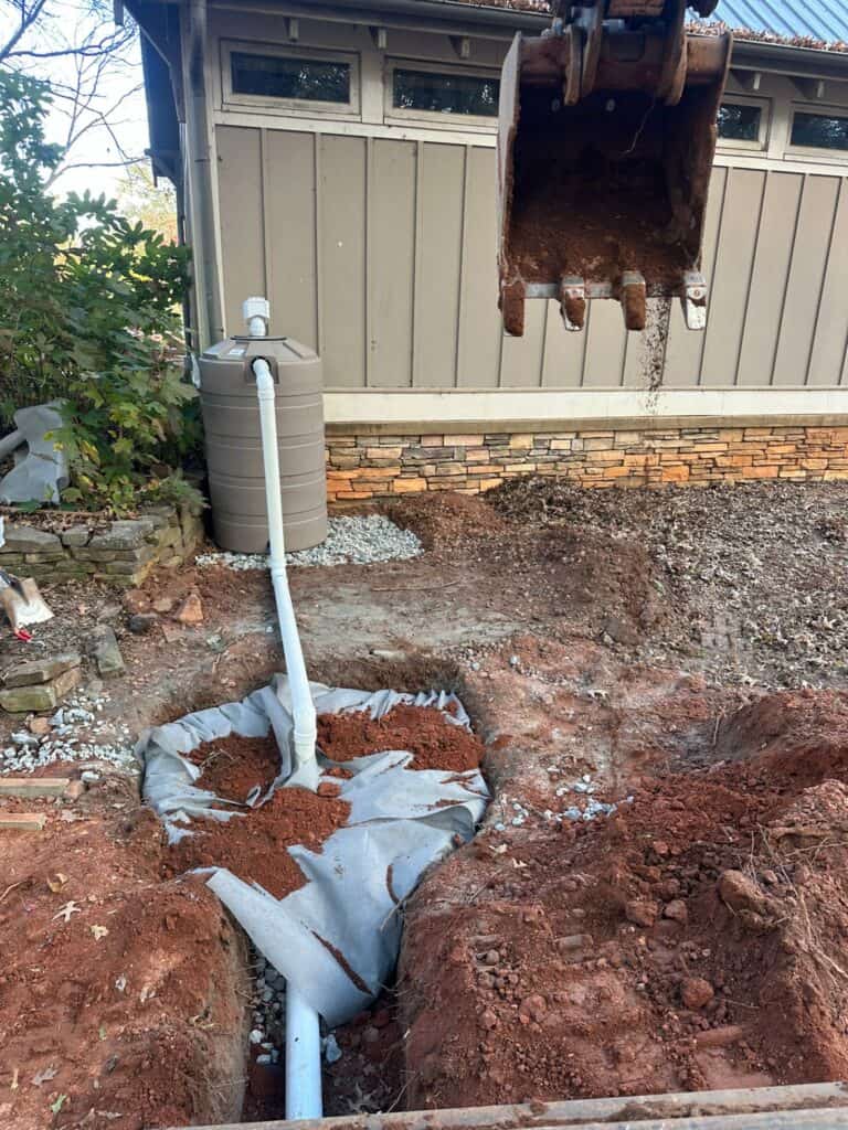 Excavator backfilling soil over the filter-fabric-wrapped dry well installation adjacent to the 200-gallon cistern at the UGA GSI demo site