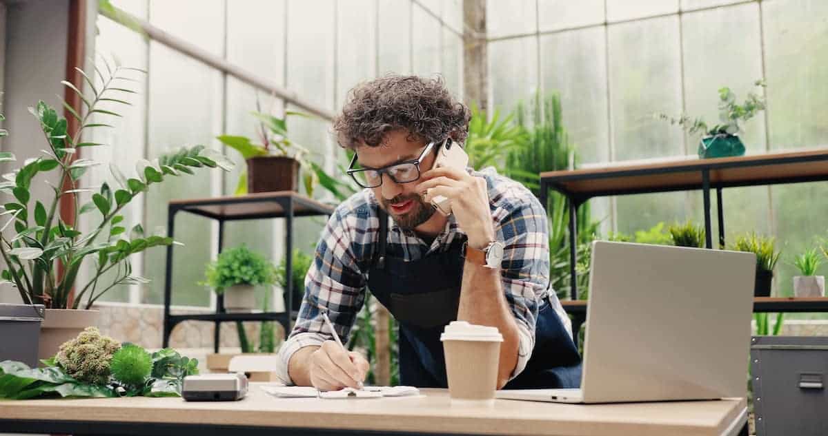 Small business owner leaning over his desk and talking on the phone