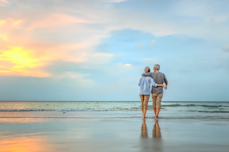 Demystifying the Life and Health Insurance License Elderly couple walking in the water on a beach with their arms around each other