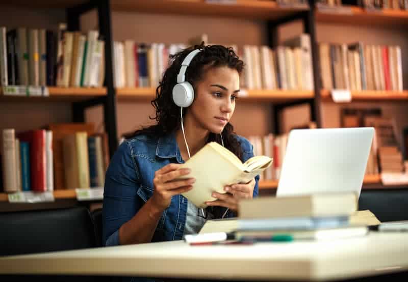 Woman Studying A woman in a library studying while wearing headphones and flipping through a book