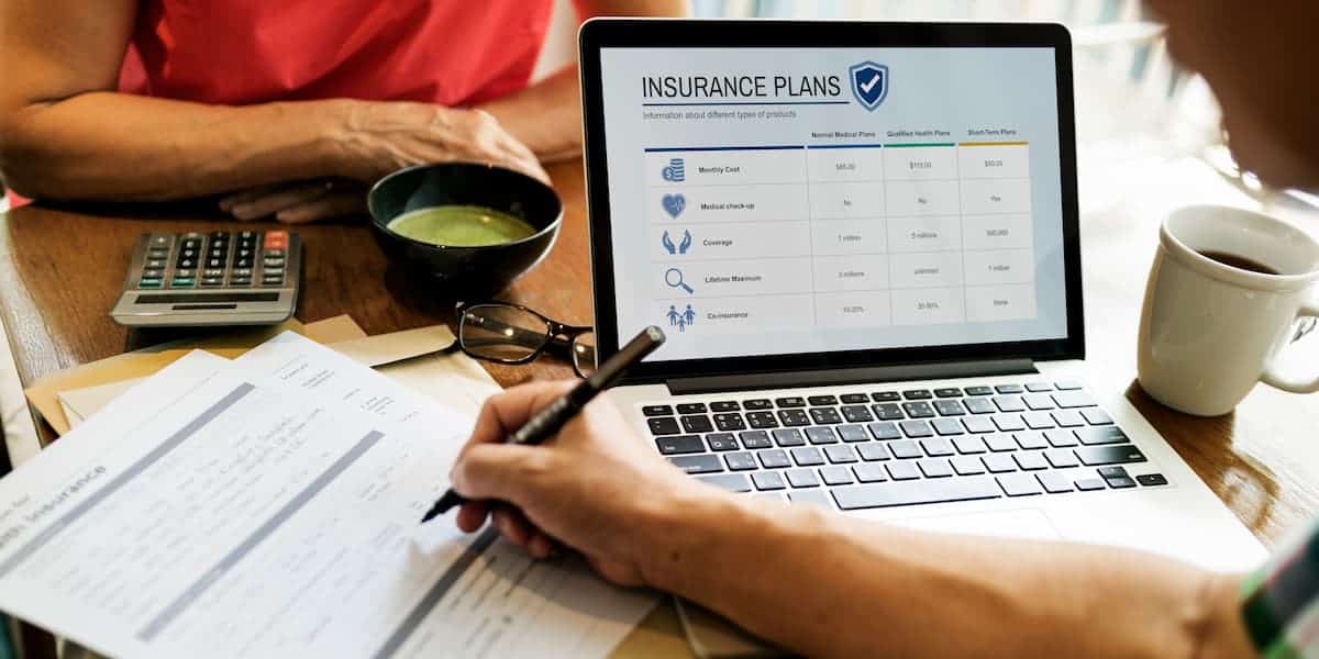 A laptop displaying a screen about insurance plan while a person writes notes
