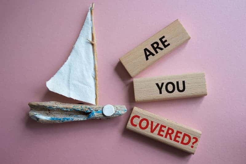 A small sailboat toy beside 3 wooden blocks with the words Are you Covered on them