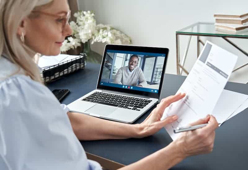 A woman digitally interviewing a candidate who can be seen on her laptop screen