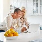 A couple leaning over their kitchen island looking at a laptop