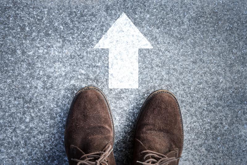 a person's feet standing on the ground with a white arrow pointing forward