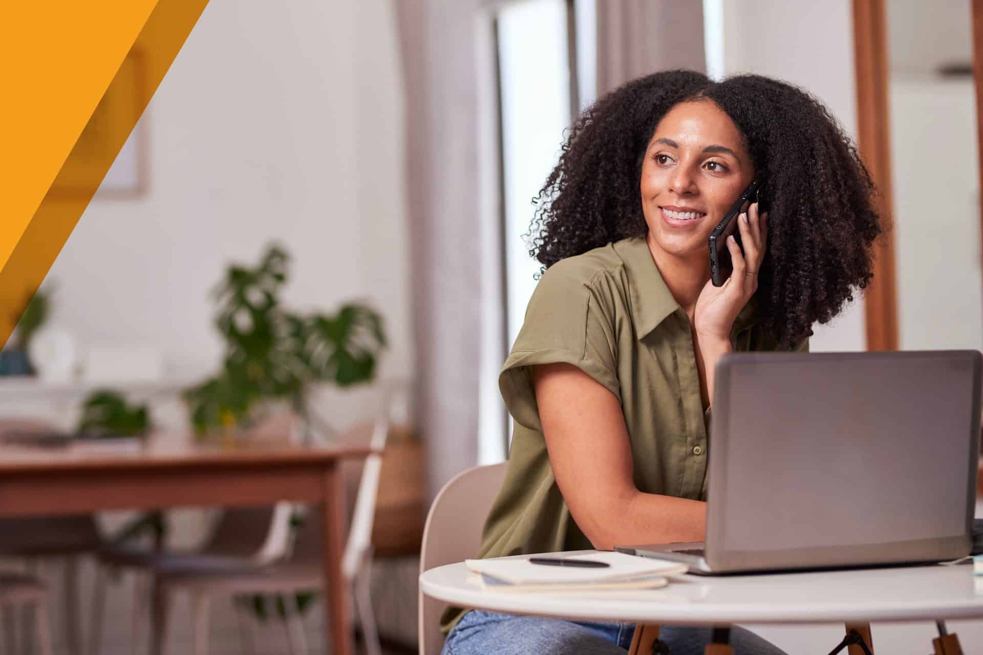 Smiling insurance agent talking on the phone at her laptop in a bright home office