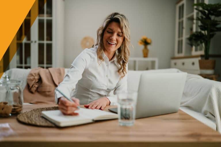 Life insurance agent working from home, smiling as she takes notes beside her laptop in a bright living room.