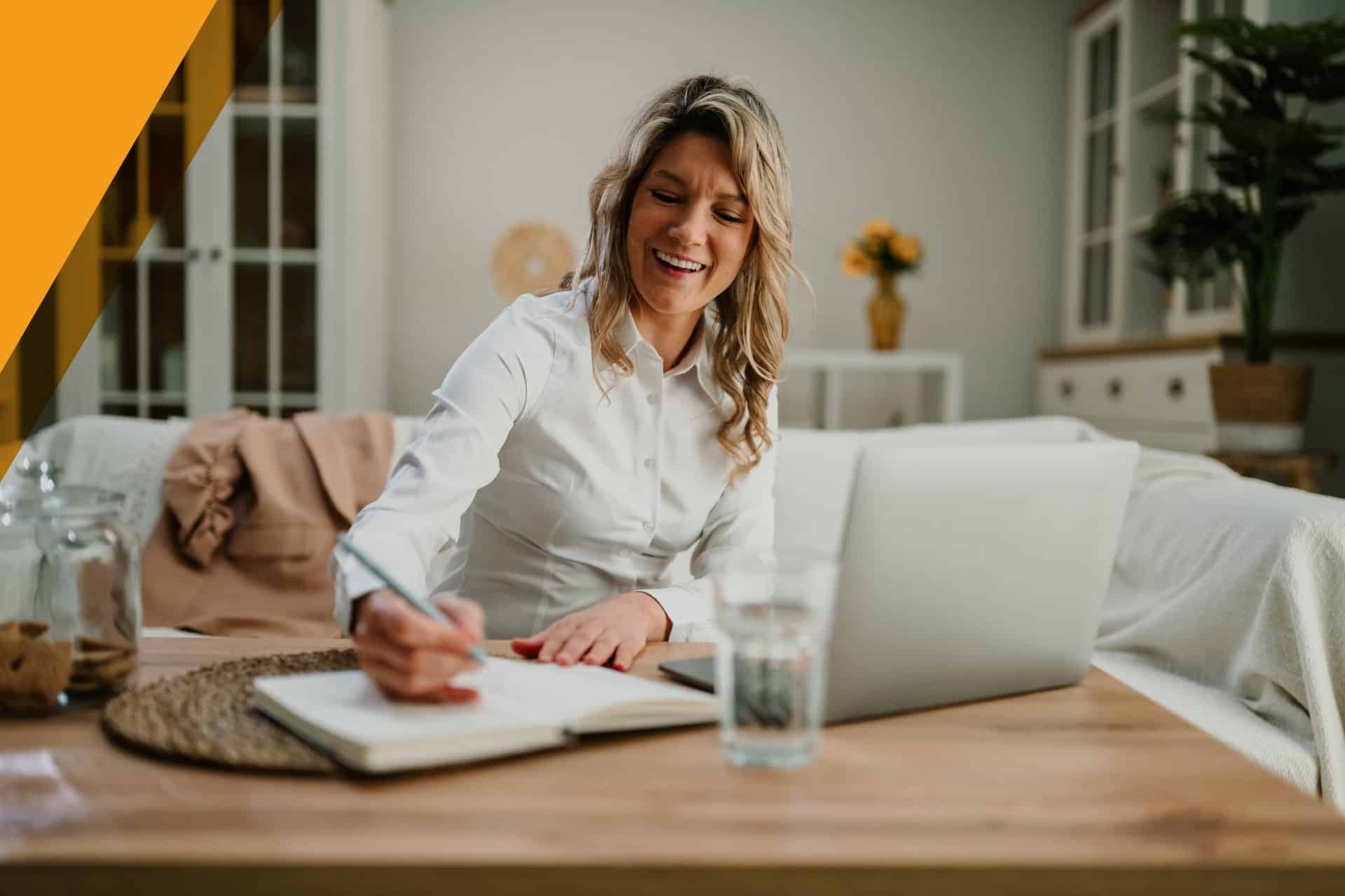 Life insurance agent working from home, smiling as she takes notes beside her laptop in a bright living room.