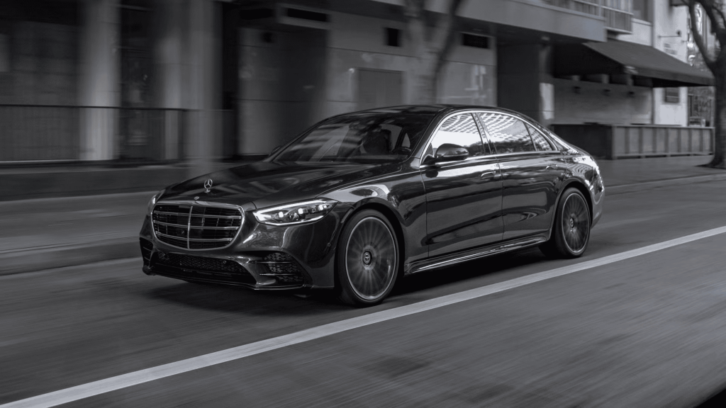 A sleek black Mercedes-Benz sedan driving on a city street, showcasing luxury and elegance.
