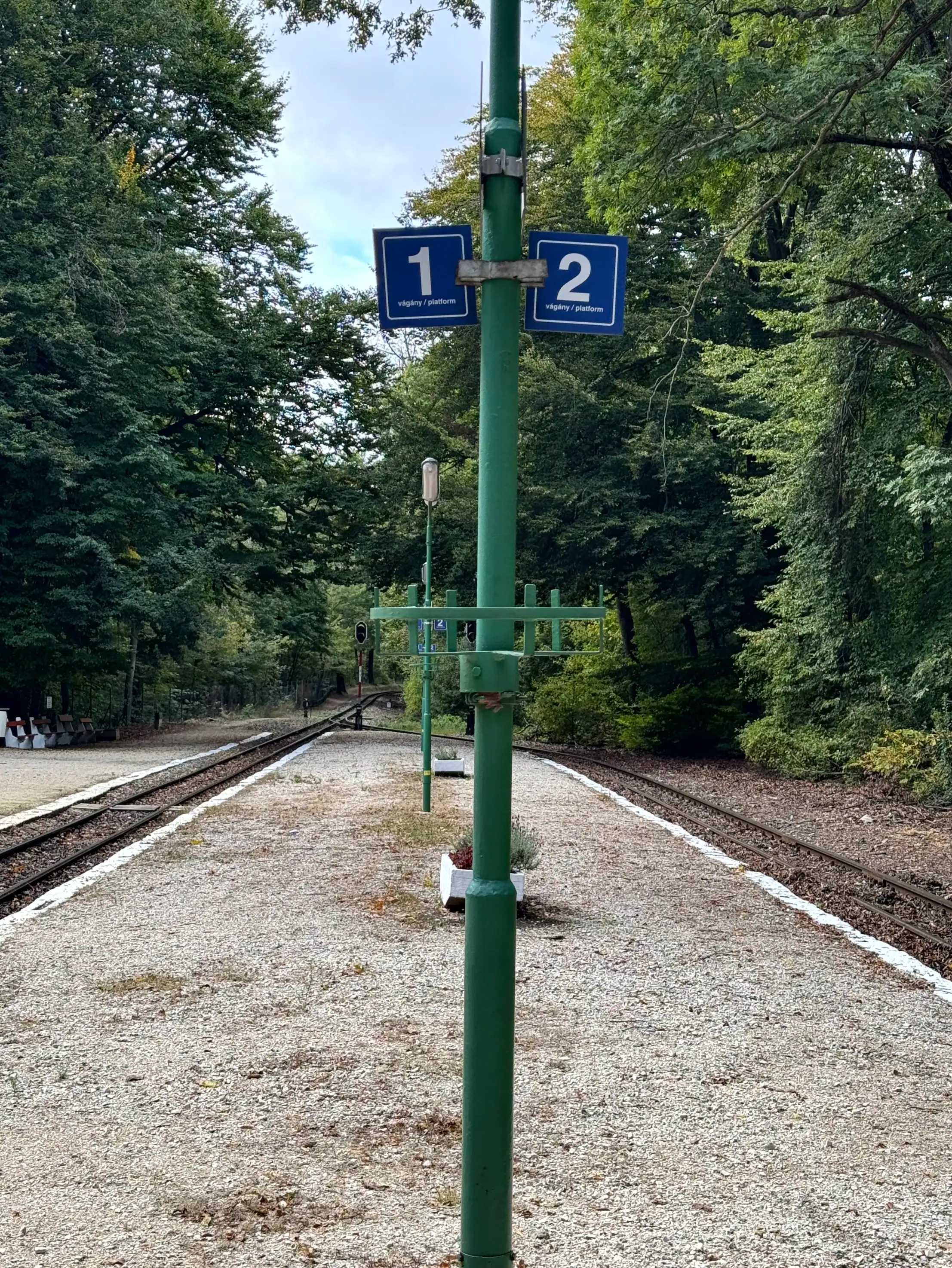 Railway station platform with track numbers 1 and 2 in a green, wooded area.
