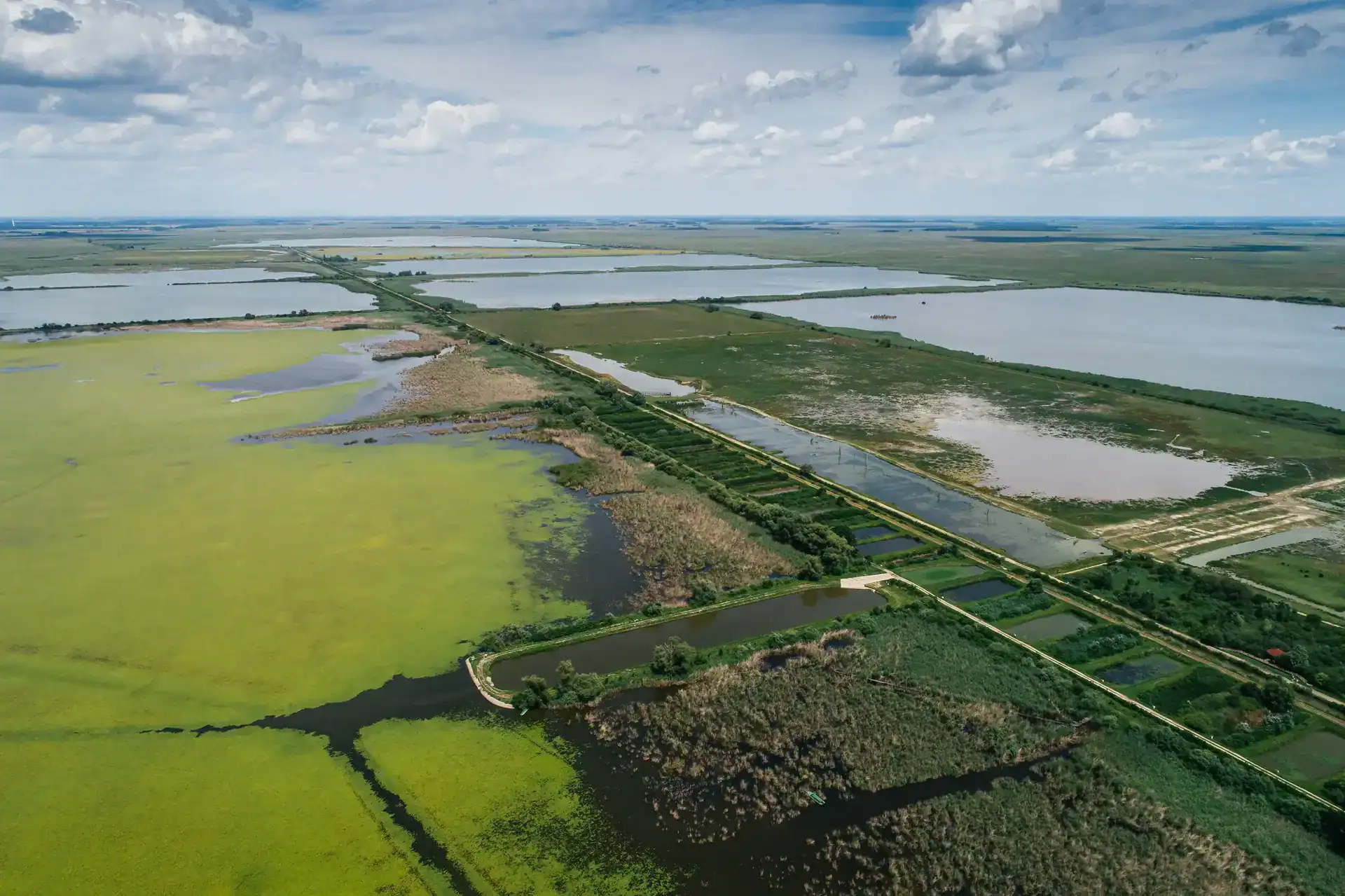 Aerial view of wetlands and lakes in Hungary with lush green areas and water bodies under a partly c.